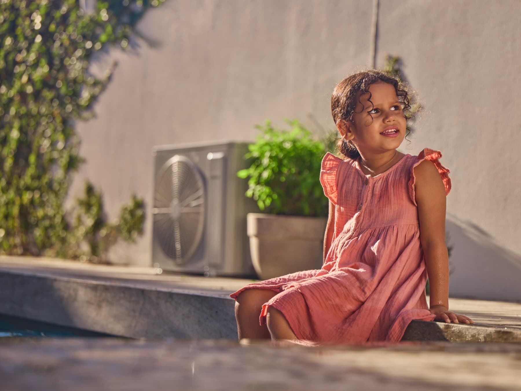 Uma menina sentada no jardim ao lado de uma bomba de calor