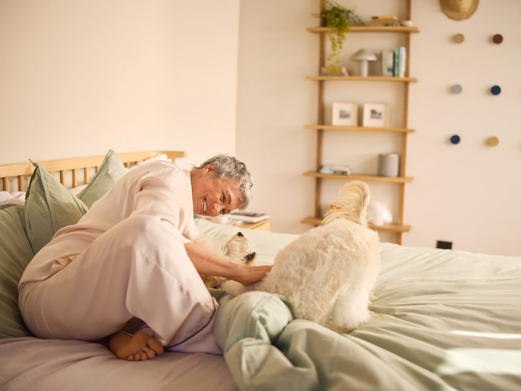Uma mulher sorridente a acariciar um cão numa cama