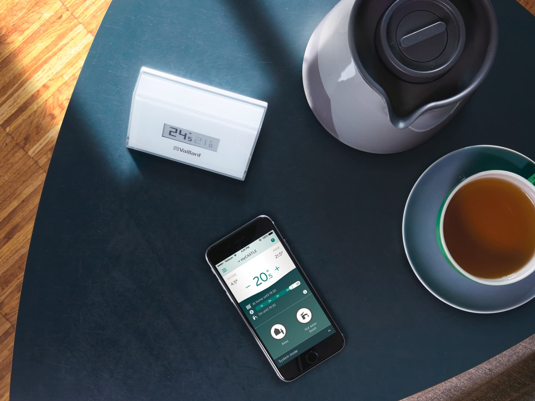 O comando da Vaillant e o smartphone numa mesinha, ao lado de uma chávena de café
