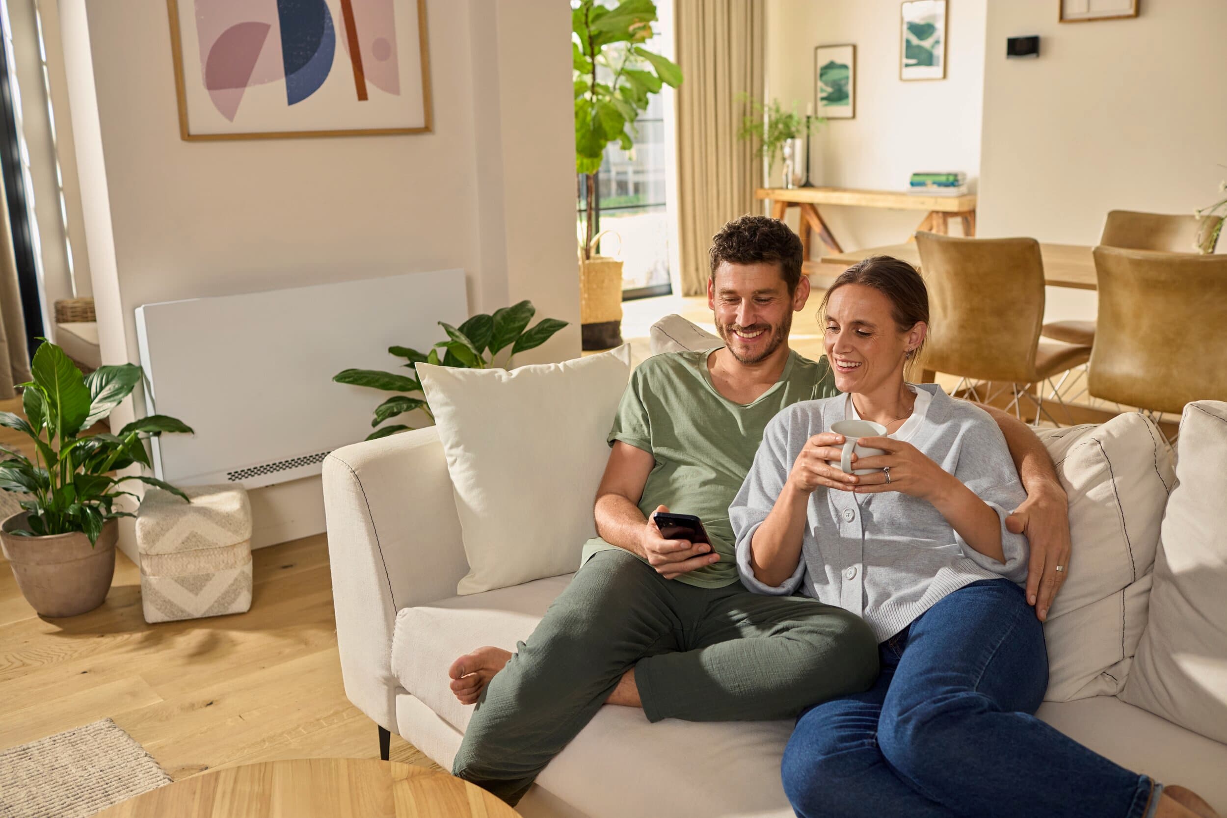 Casal a relaxar no sofá, com uma unidade de ventilação e refrigeração aroVAIR plus ao fundo