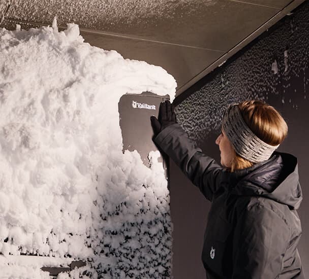 Mulher a limpar a neve de uma bomba de calor