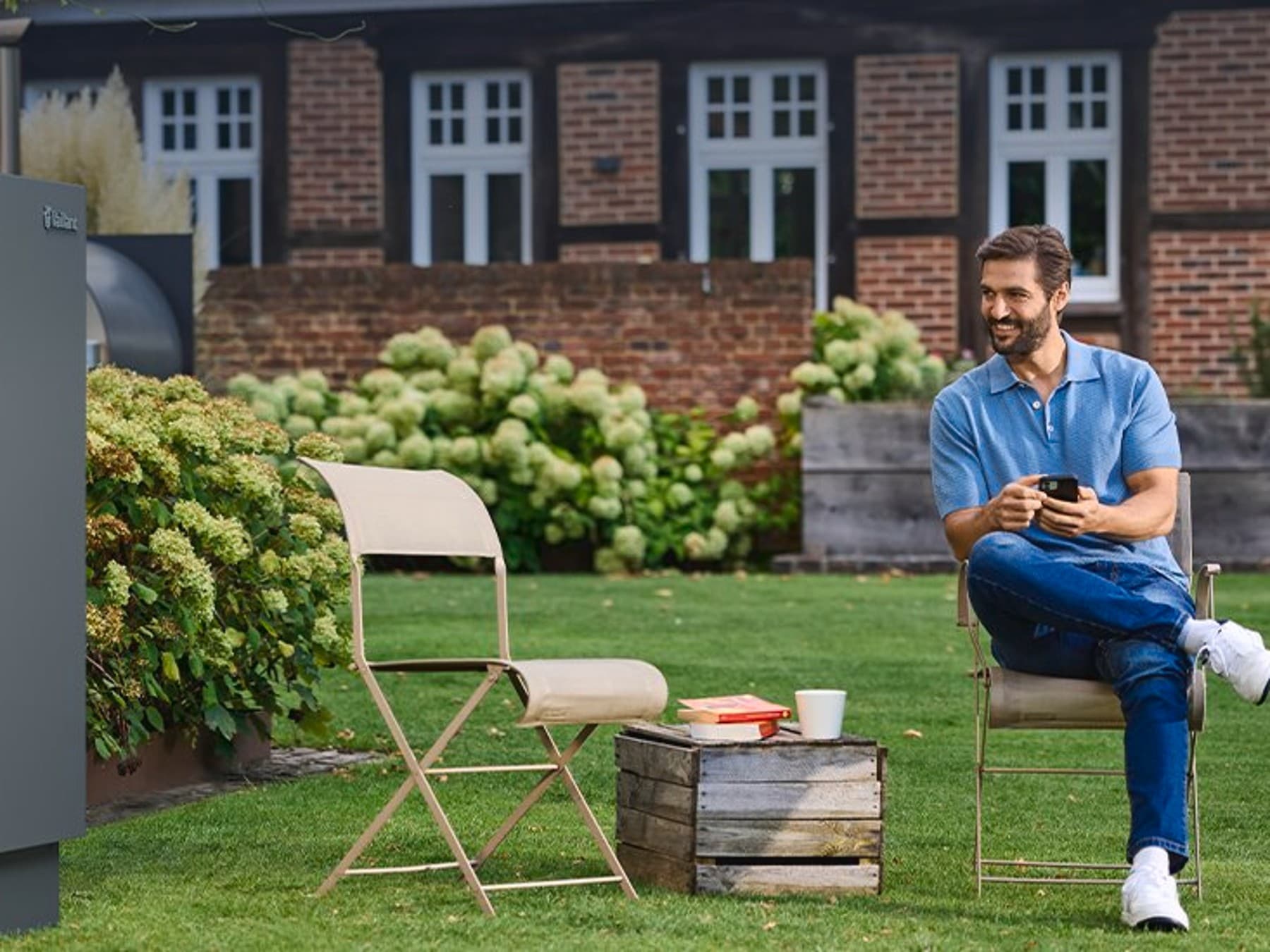 Homem sentado no seu jardim ao lado de uma unidade exterior aroTHERM plus