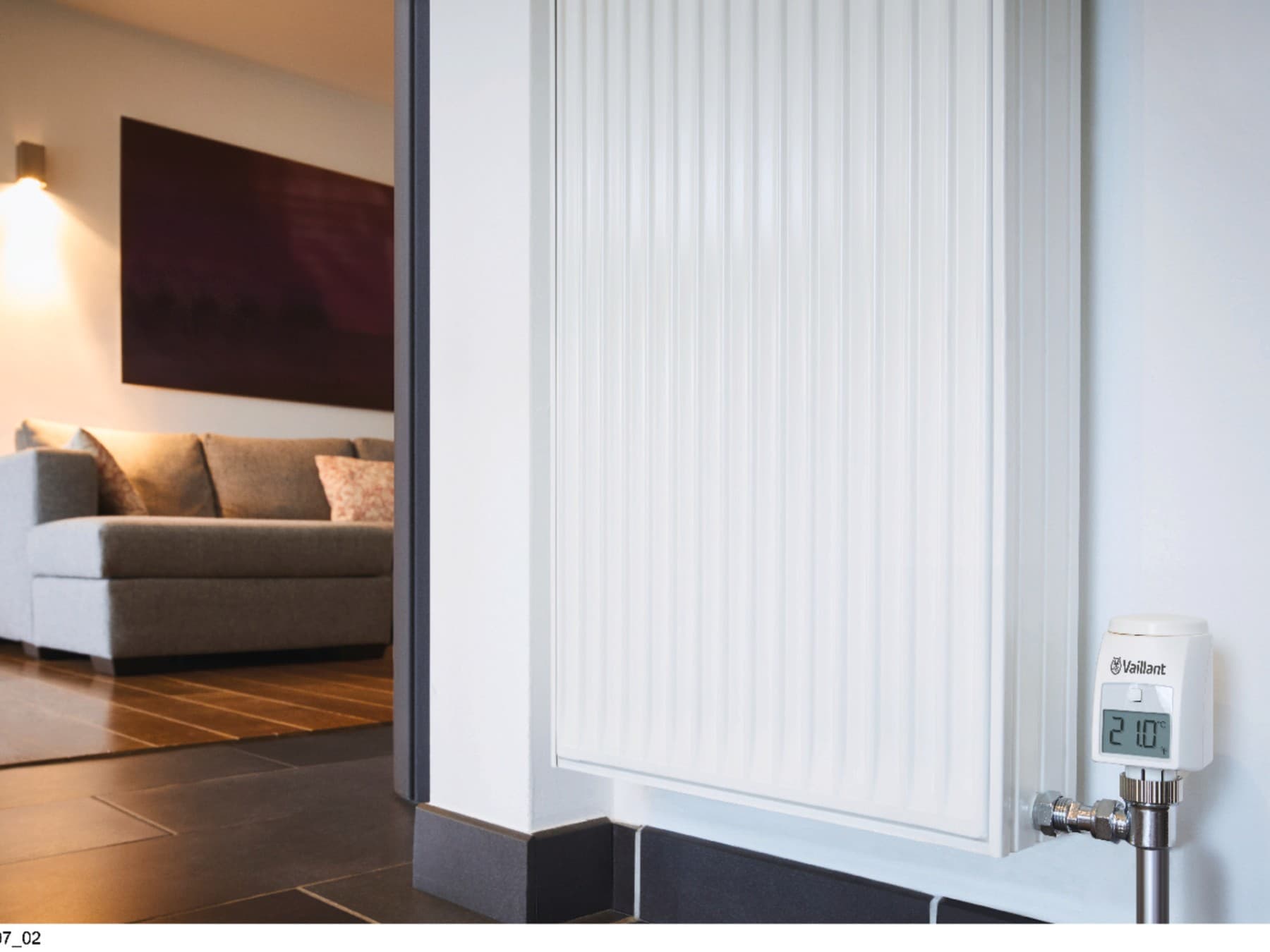 Um radiador com um sofá e uma luz aconchegante ao fundo, o visor do radiador mostra 21 °C.